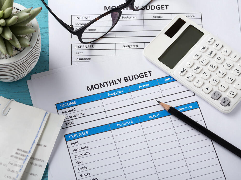 Calculator, pencil, receipts and monthly budget sheets on a table.