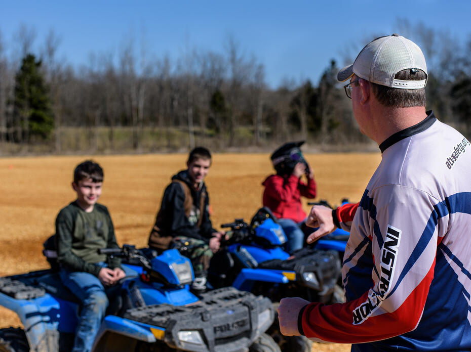 Three young people sit on ATVs as they listen to their instructor.
