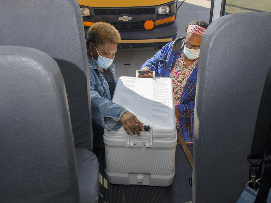 Two women load an ice chest on a bus.