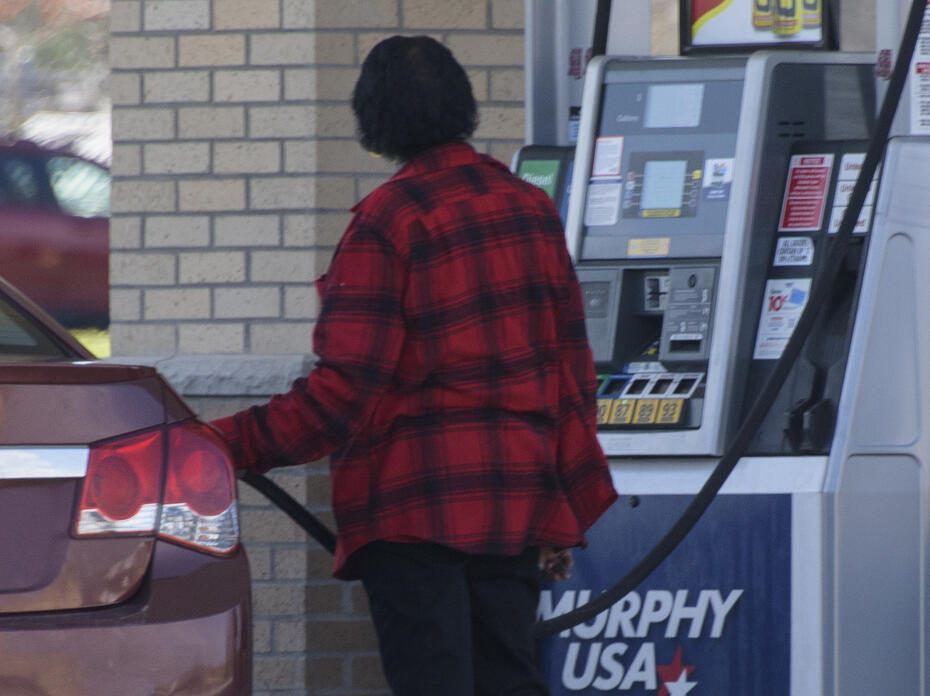 An adult pumps gas into a car at a gas station.