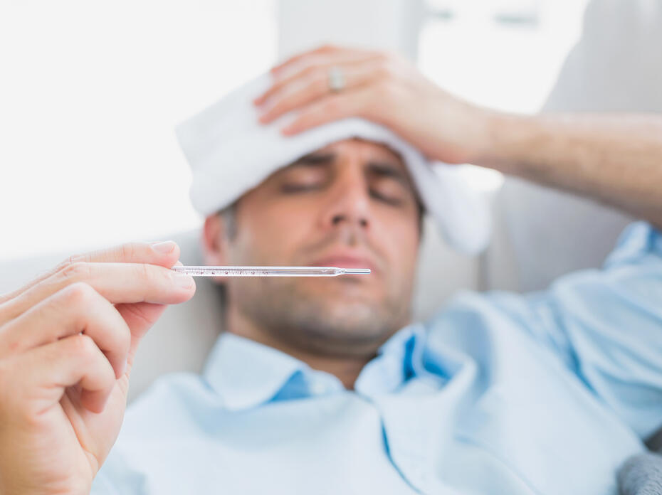 Sick man lying on sofa checking his temperature at home in the living room