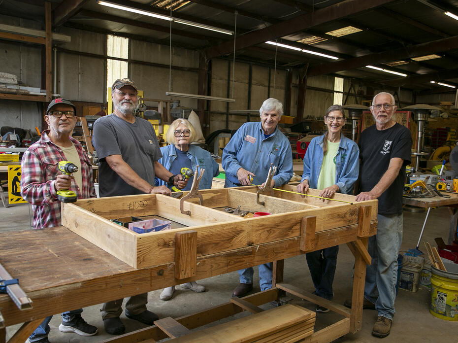 A group of people stand in a shop around a woodwork project.