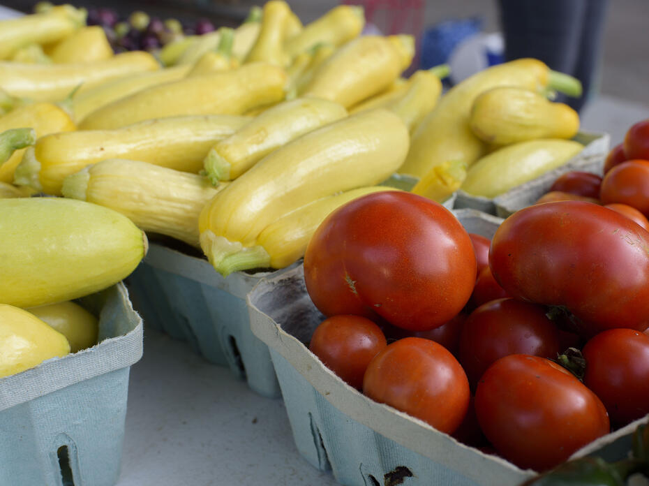Close up of tomatoes and yellow squash in farmers market baskets.