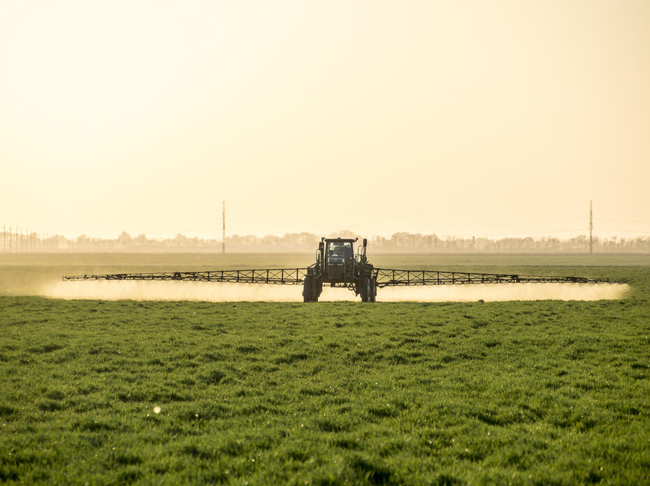 A tractor with a boom arm sprays crops.