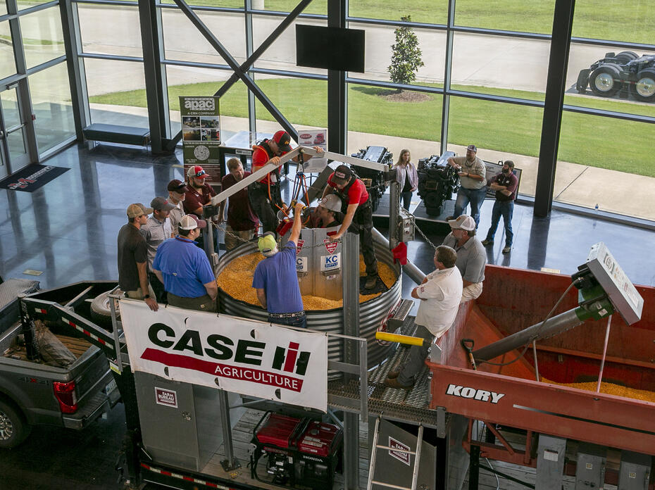 Overhead shot of a dozen people peering into a grain bin with one person inside.