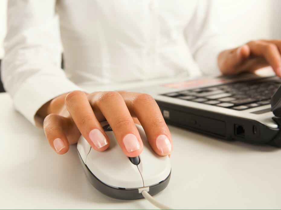 A person’s right hand rests on a computer mouse while their left hand rests on a laptop keyboard.