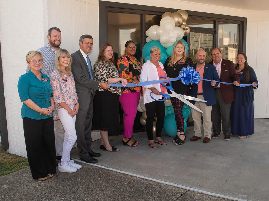 A group of people hold a ribbon in front of a building entrance.