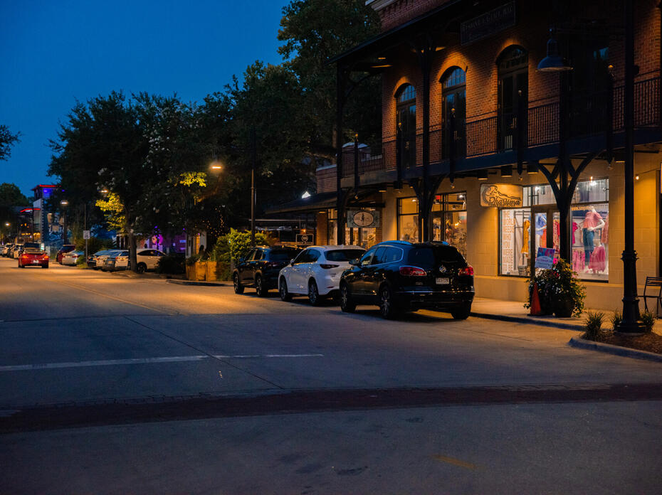 A night view of a downtown street in Ocean Springs, Mississippi, lined with shops and parked cars.