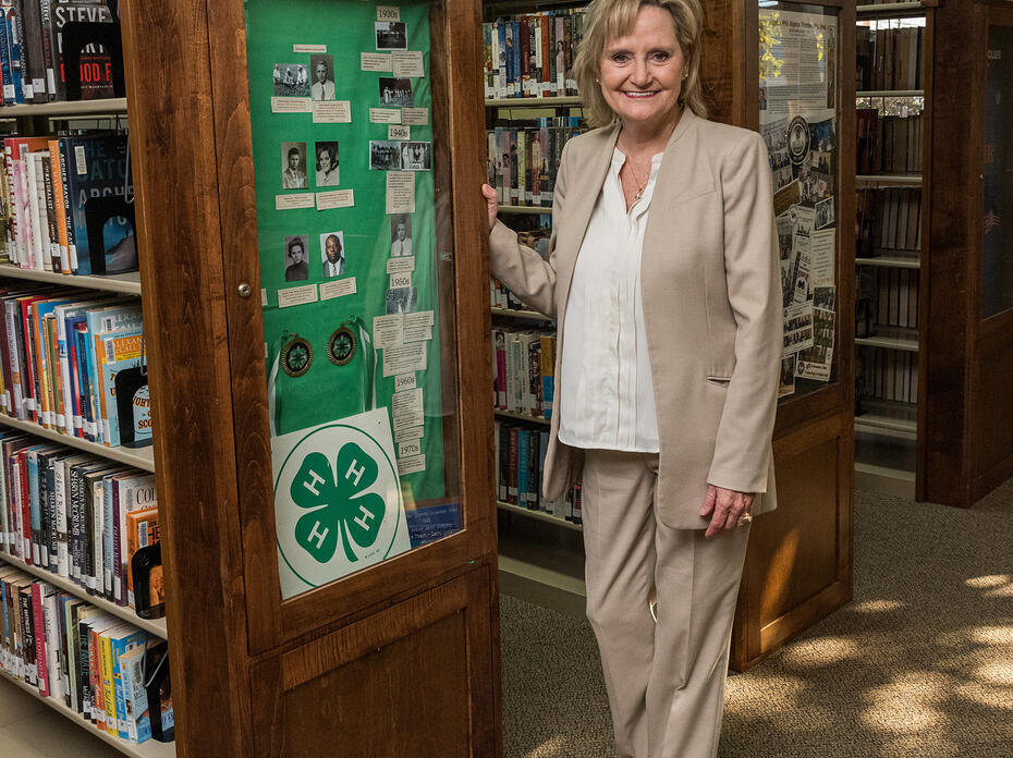 U.S. Senator Cindy Hyde-Smith stands next to a display case in a library.
