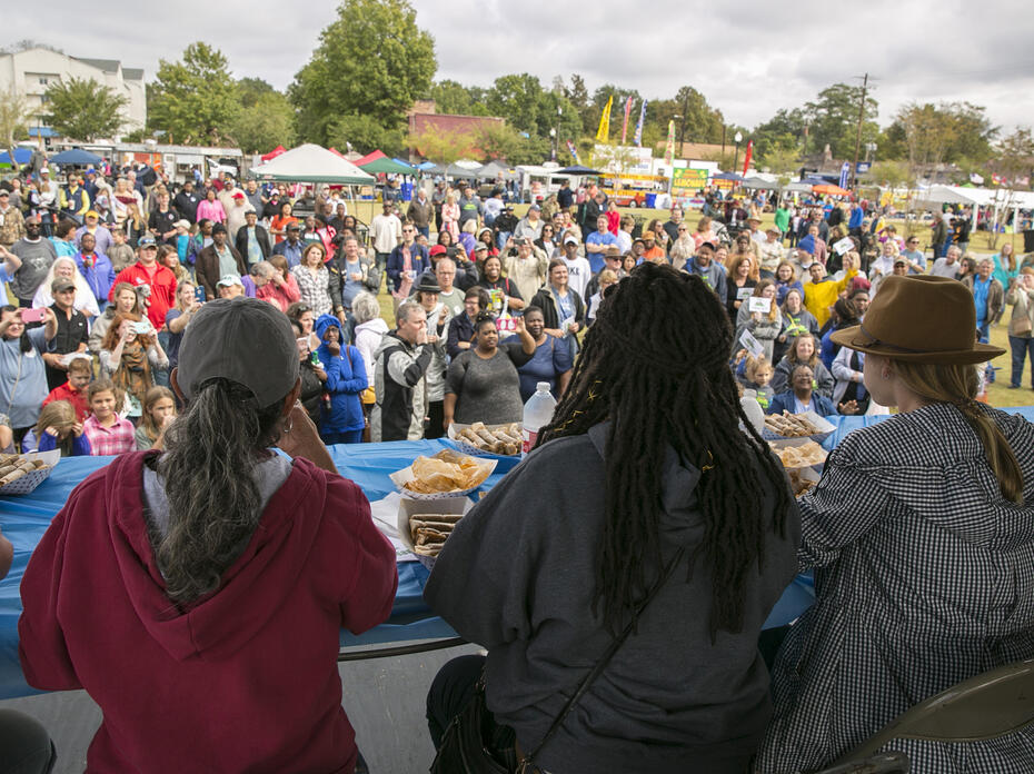 A large crowd gathers at a festival while a panel of judges tastes food.