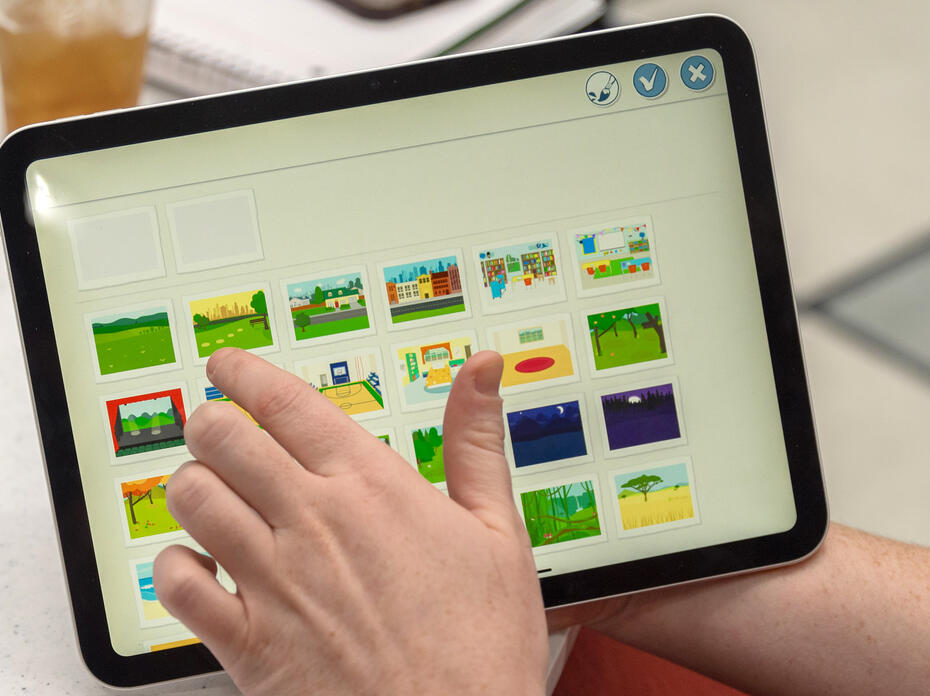 A hand touching the screen of a tablet to pick a picture from a selection.