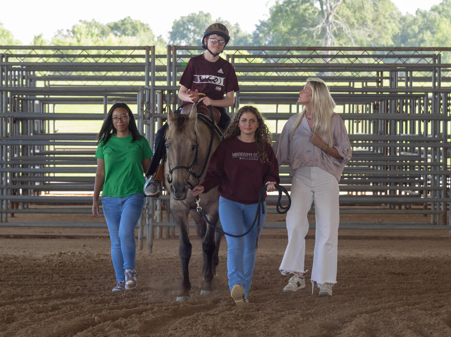Boy riding a horse surrounded by three people.