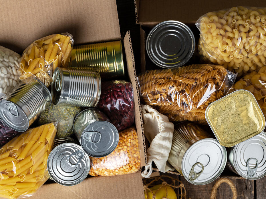 A box of food to donate, including beans, pasta, and canned goods.