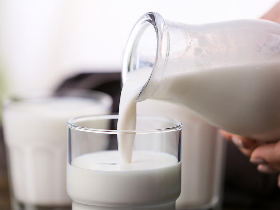 Hand pours milk from a glass bottle into a cup