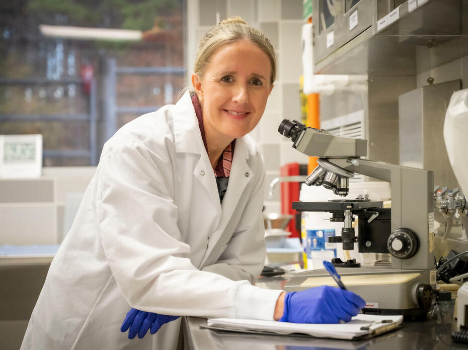 Doctor in a white coat smiling and standing beside a microscope