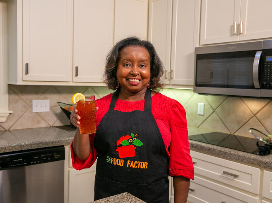 A woman holds a glass of strawberry gree tea in a kitchen.