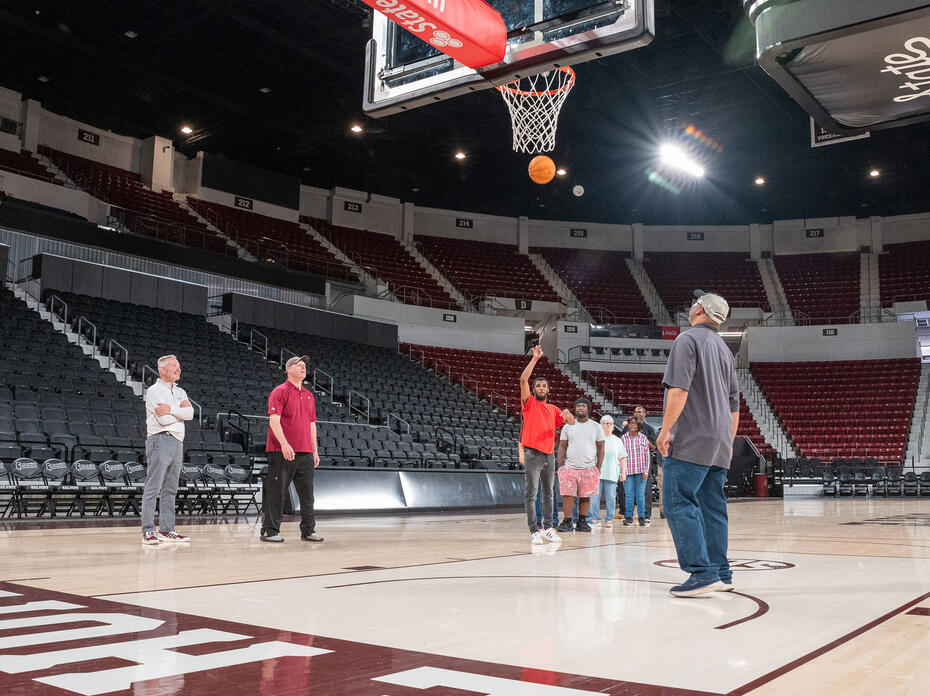 One man shoots a basketball on a court as others stand nearby.
