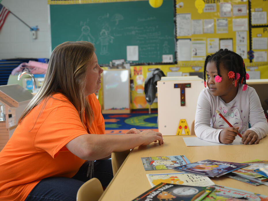 A teacher speaks to a child in a classroom.