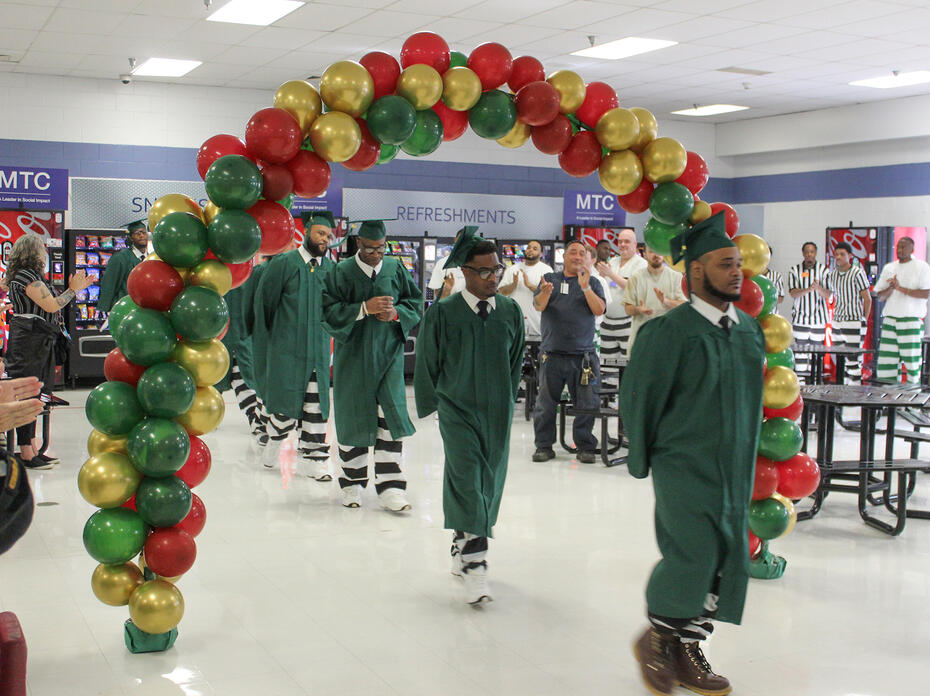 Graduates in gowns walk under a balloon arch.
