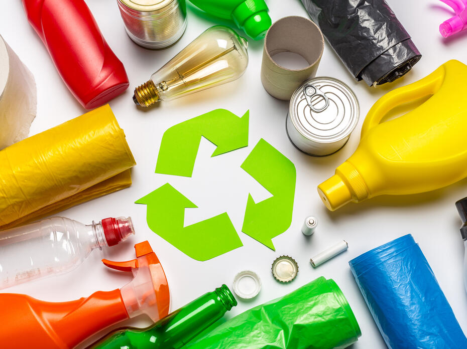 Several types of plastic and other waste surround a green chasing arrows emblem.