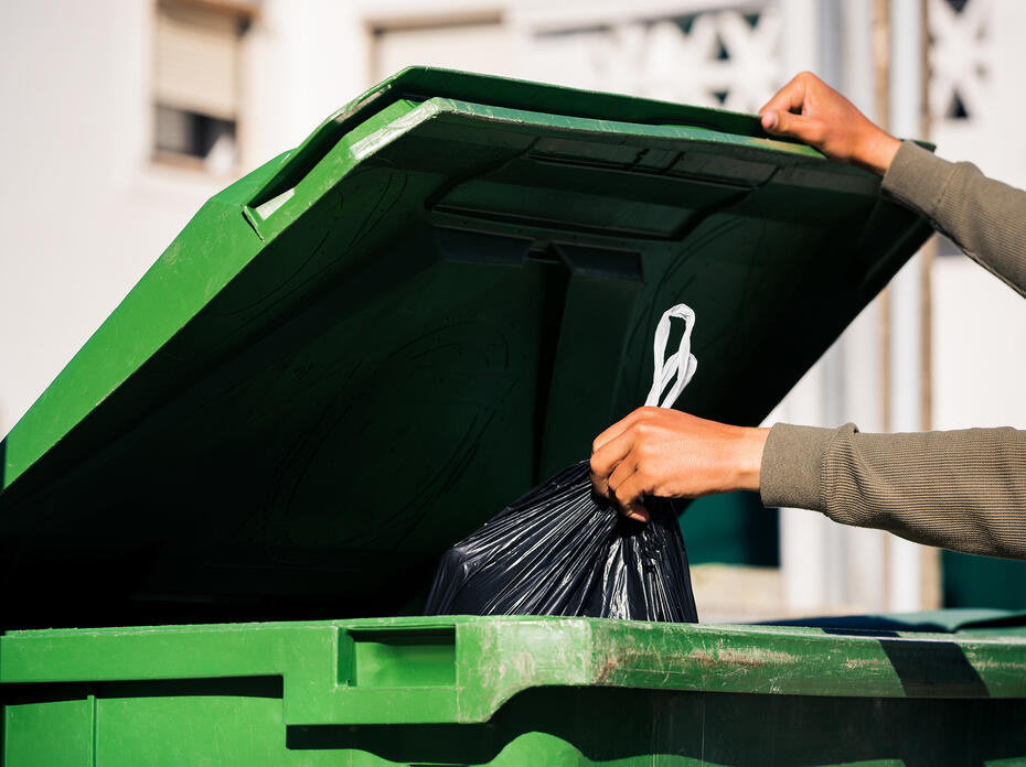 A person throwing a trash bag into a trash can.