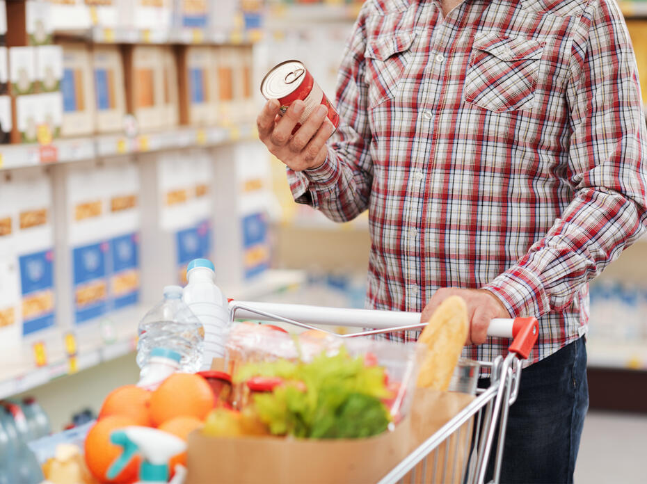 A person reads a Nutrition Facts label on a can of food in the grocery store.