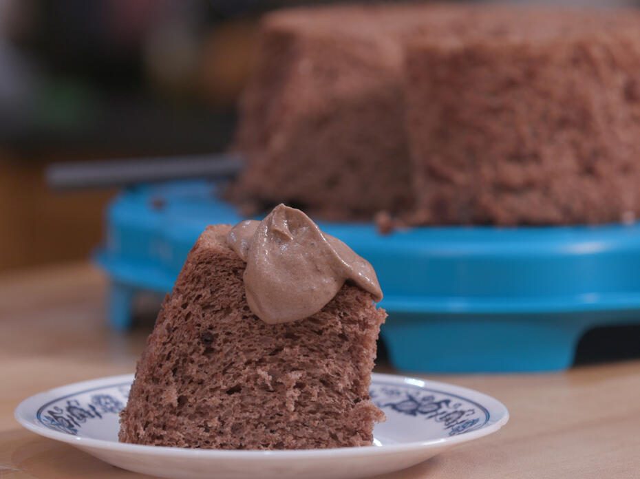A slice of chocolate angel food cake on a small saucer with the entire cake on a blue platter in the background