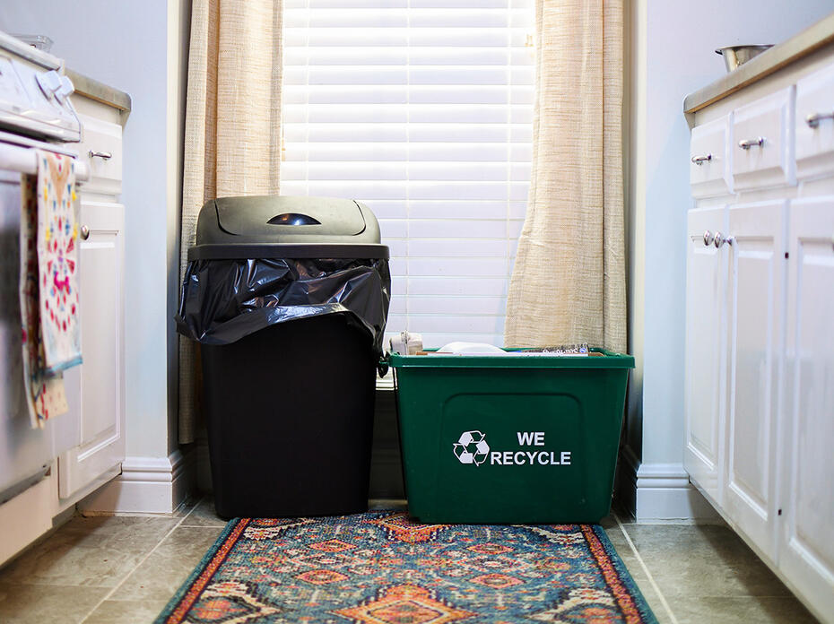 A green recycling bin sitting next to a black trashcan. 