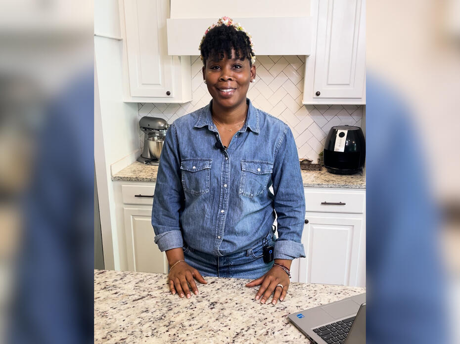 A woman standing at a kitchen counter smiles at the camera.