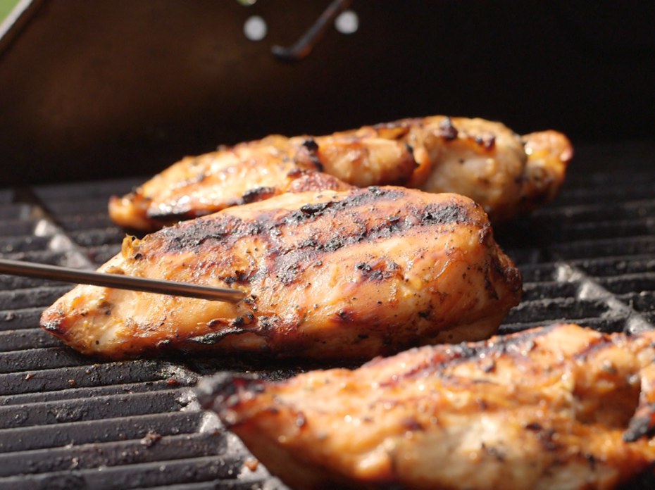 Hand with meat thermometer chicken middle of 3 chicken breasts on outdoor grill.