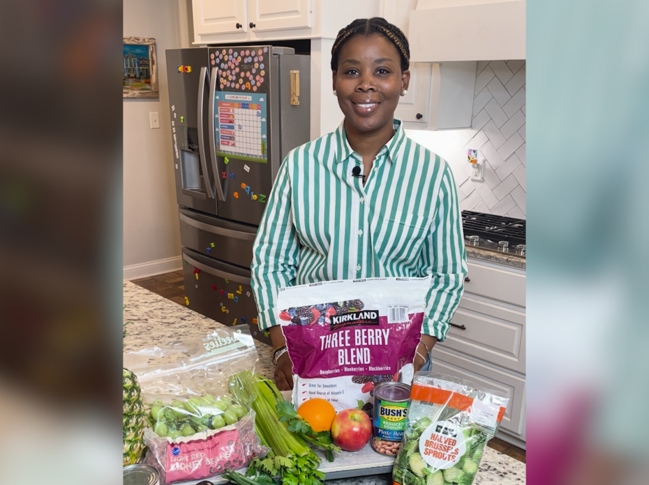 A woman stands behind a kitchen counter with a variety of foods displayed.