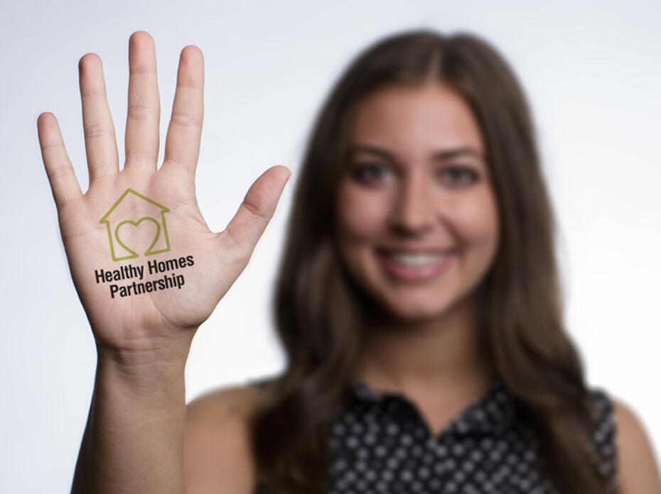 A young woman with dark hair extends her palm forward with the Healthy Homes Initiative logo on her palm.