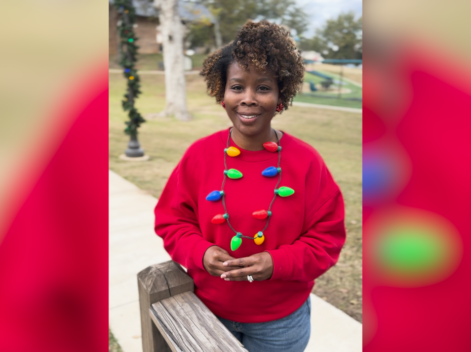 A woman stands on a sidewalk in a red sweatshirt and festive holiday-themed necklace.
