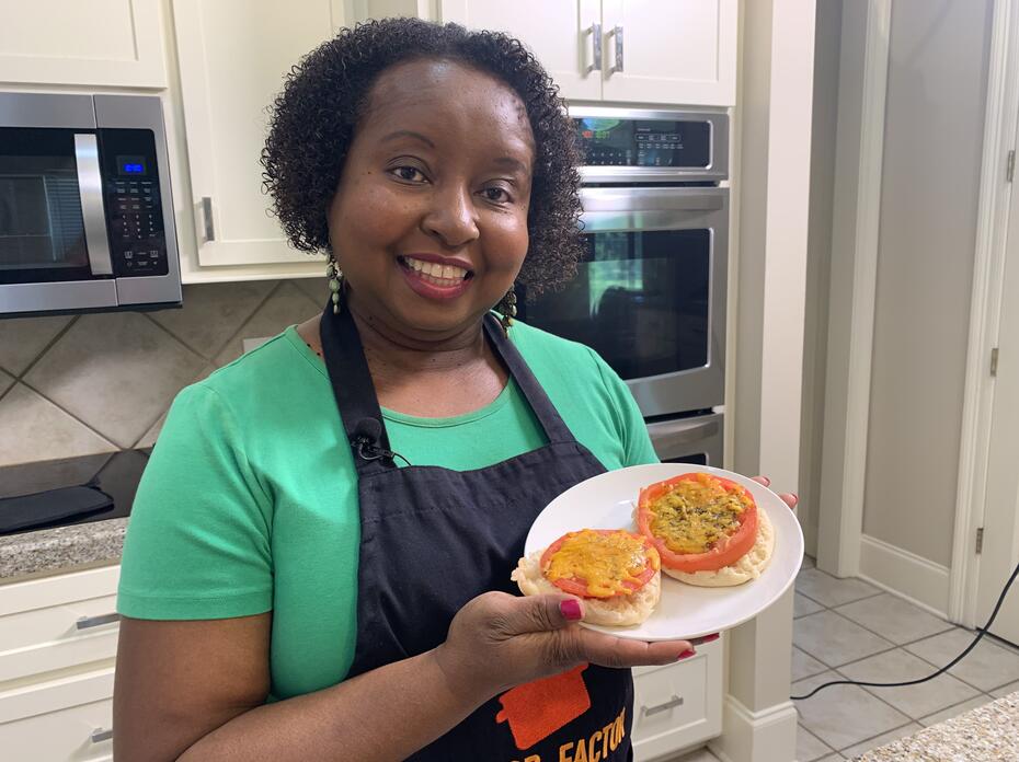 A woman stands in a kitchen holding a plate of prepared Baked Tomatoes with Cheese.