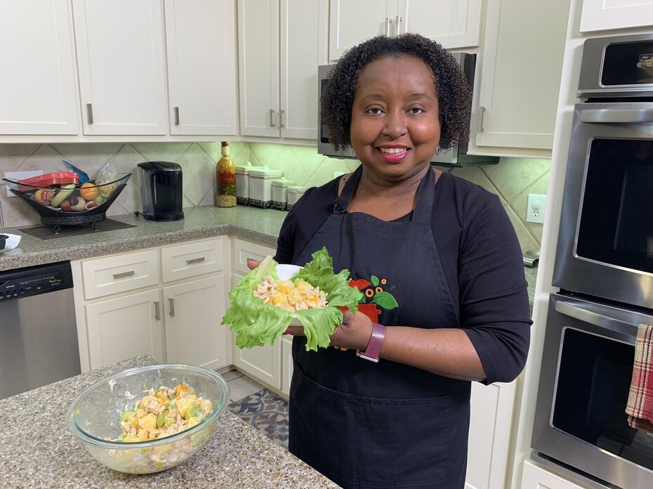A woman holds a bowl of chicken and fruit salad.