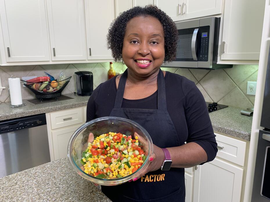A woman holds a bowl of corn and cucumber salad.