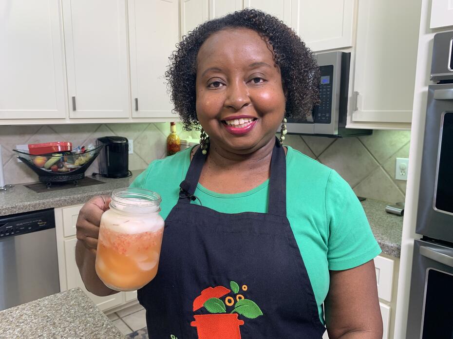 A woman in a kitchen holds a glass of strawberry pineapple lemonade.