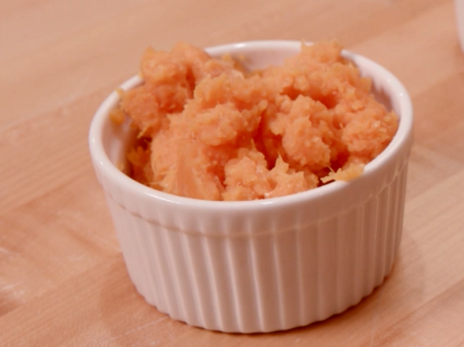 Mashed sweet potatoes in a white ceramic ramekin on a butcher block table.