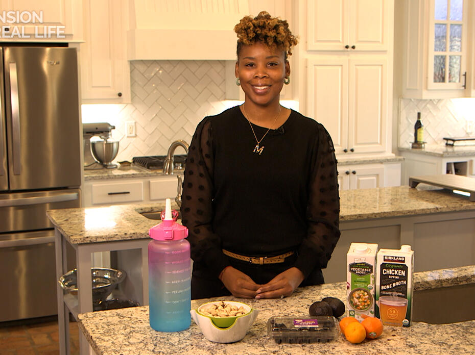 A woman stands behind a kitchen counter with food items displayed.