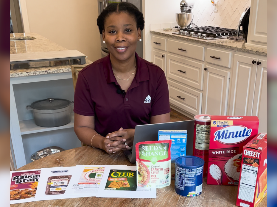 A woman sits at a table with various food products with Nutrition Facts labels displayed.