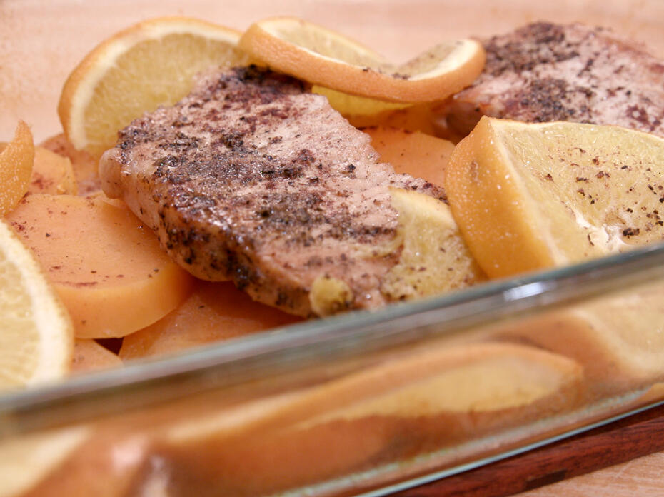 Baked boneless porkchops on sliced sweet potatoes topped with orange slices in a glass baking dish