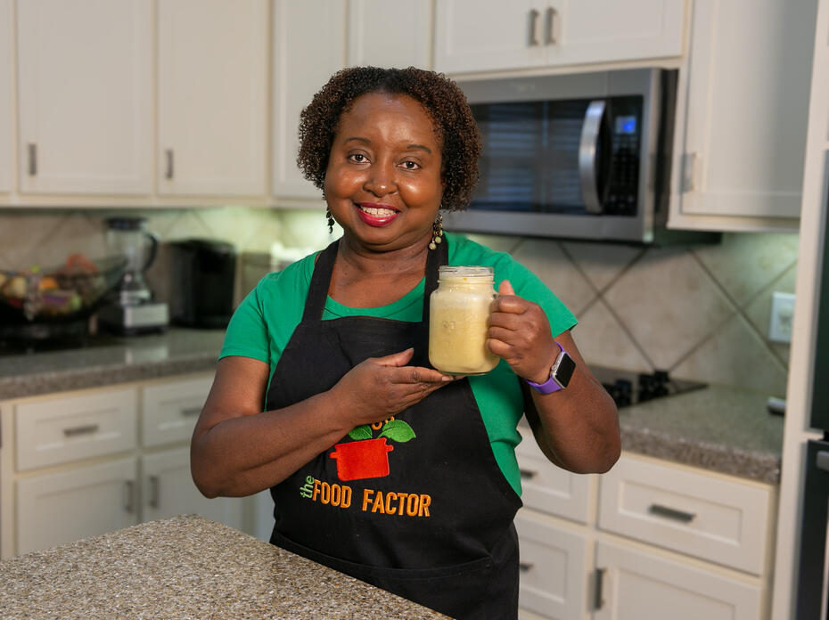 A woman stands in a kitchen holding a glass of peach cooler for the camera.