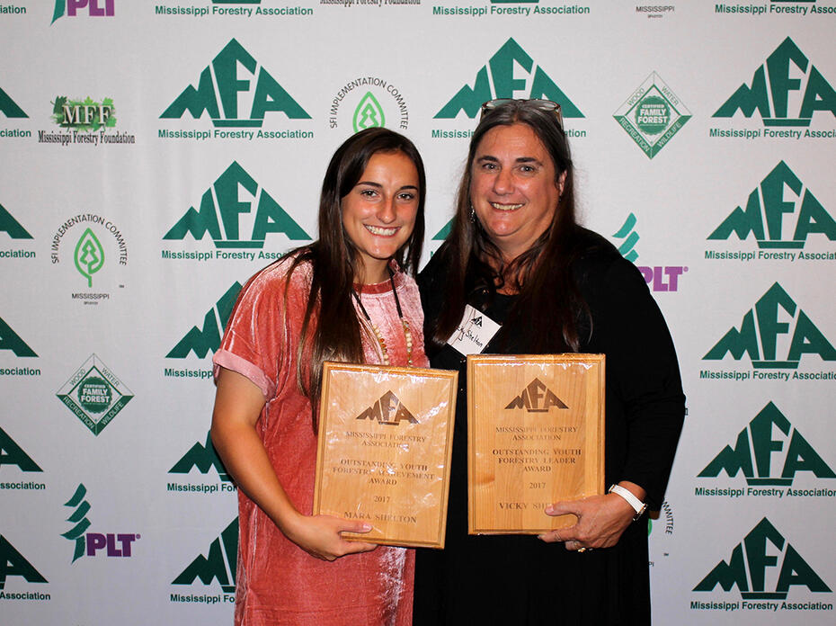Two women stand while holding award plaques at the Mississippi Forestry Association annual meeting. 