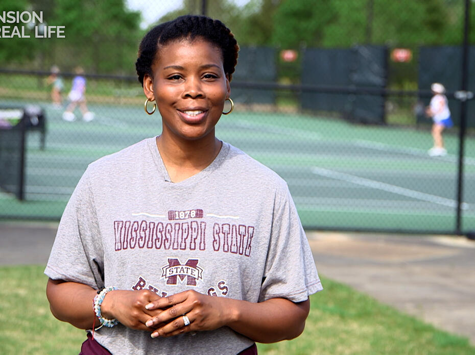 A woman stands in front of a tennis court