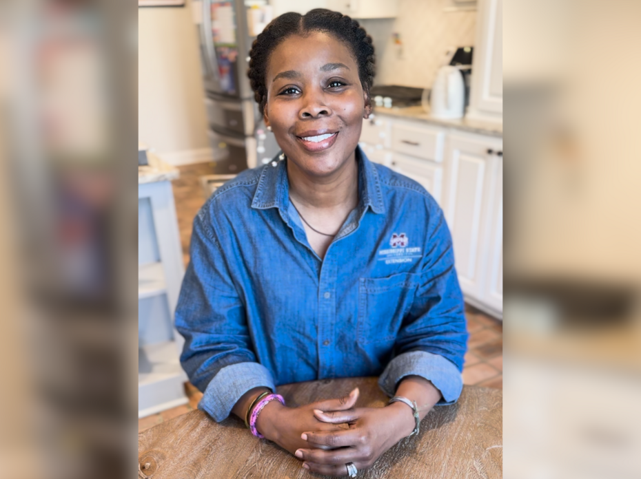 A woman sits at a kitchen table and smiles for the camera.
