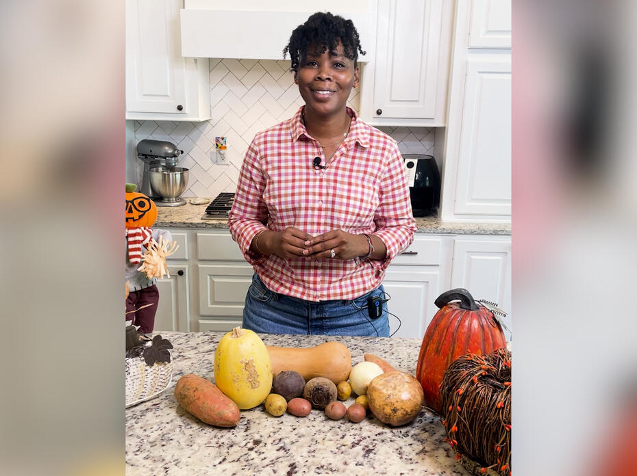 A woman stands in a kitchen with various root vegetables on the counter.
