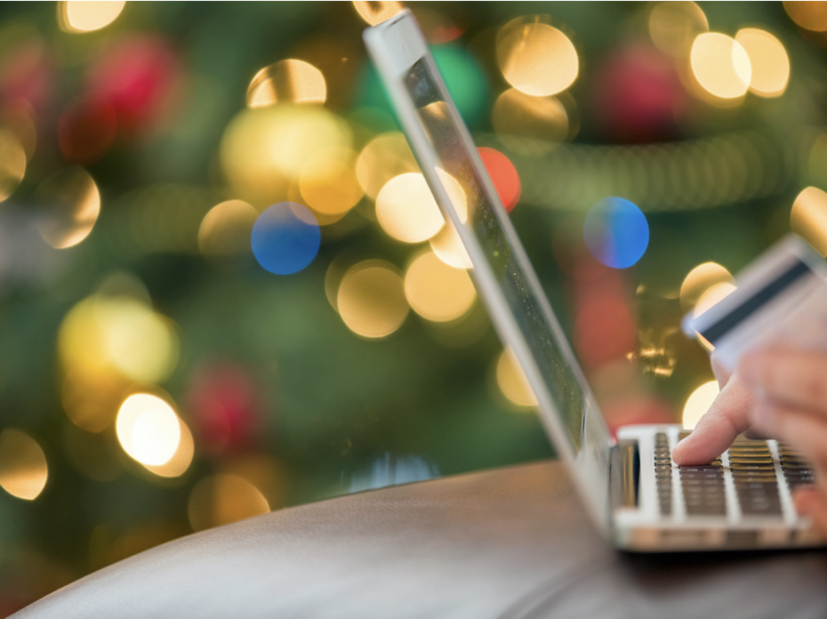 Close up view of a person ordering merchandise from a laptop computer in front of a Christmas tree.