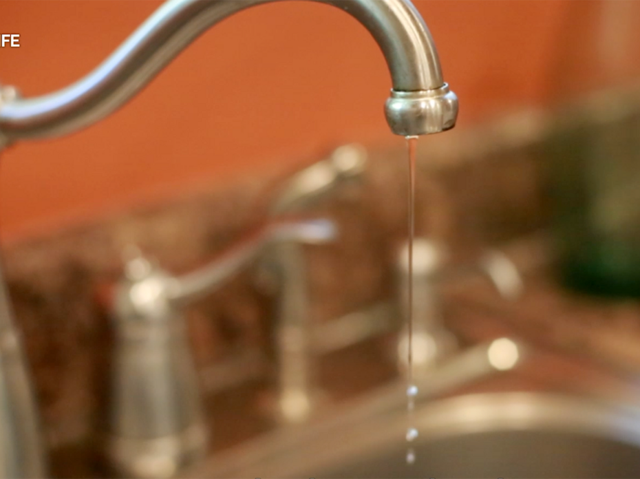 A thin stream of water drips from a stainless steel kitchen sink faucet.