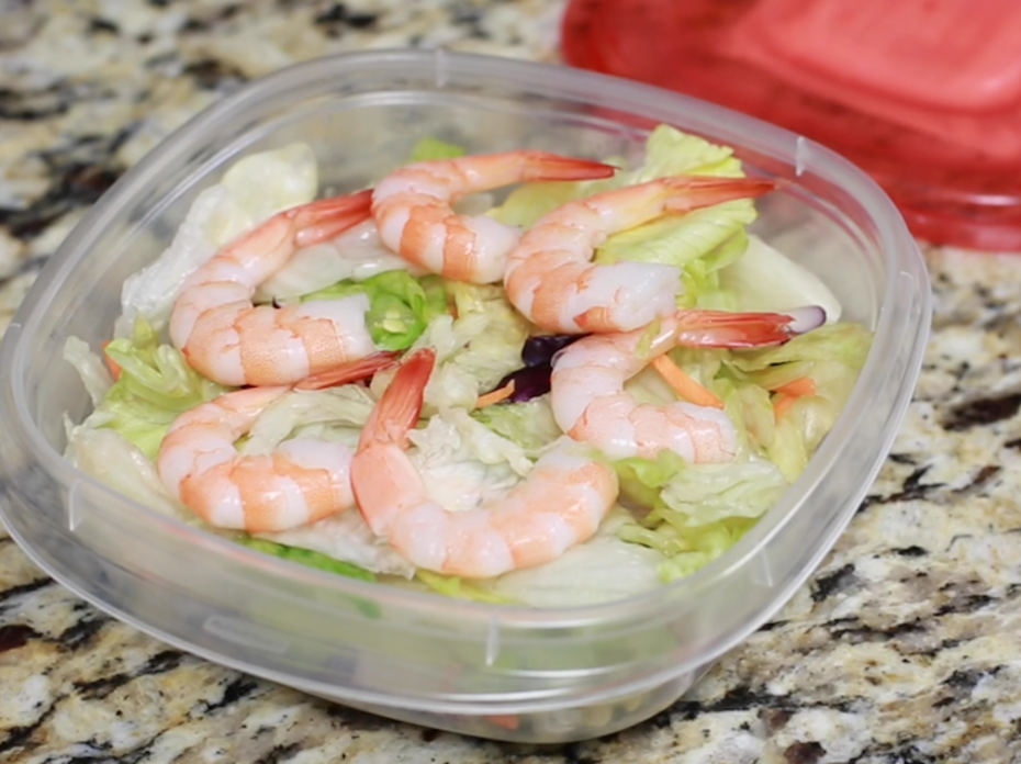A bowl of salad with shrimp on top. 