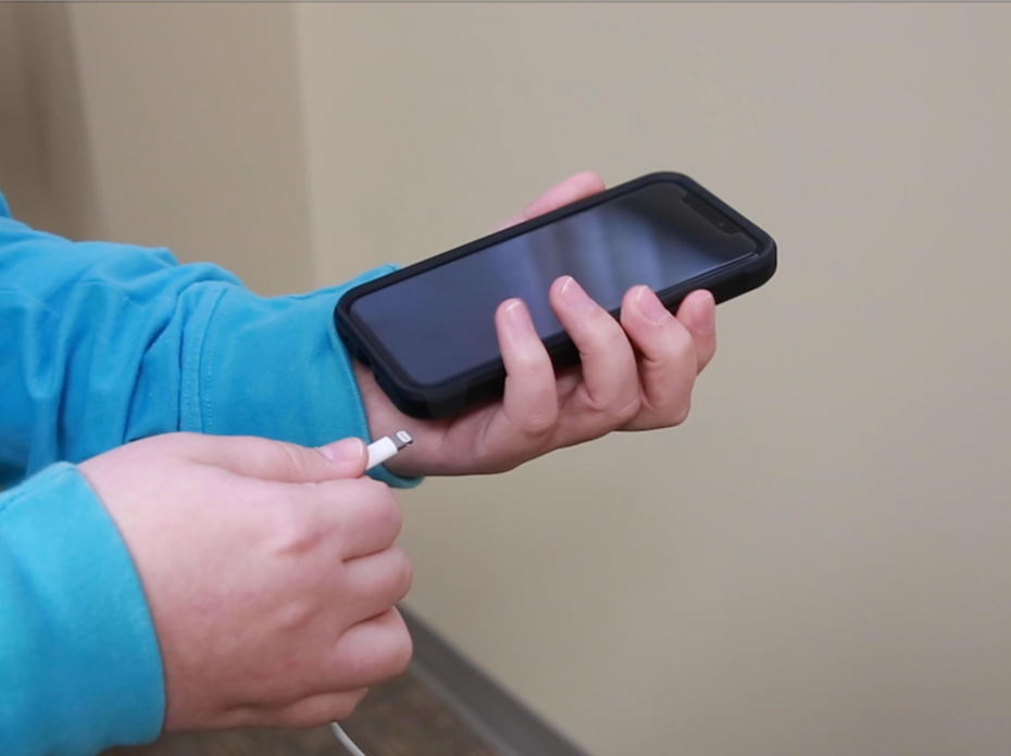 Pair of hands holding the power cord and an unplugged smart phone.